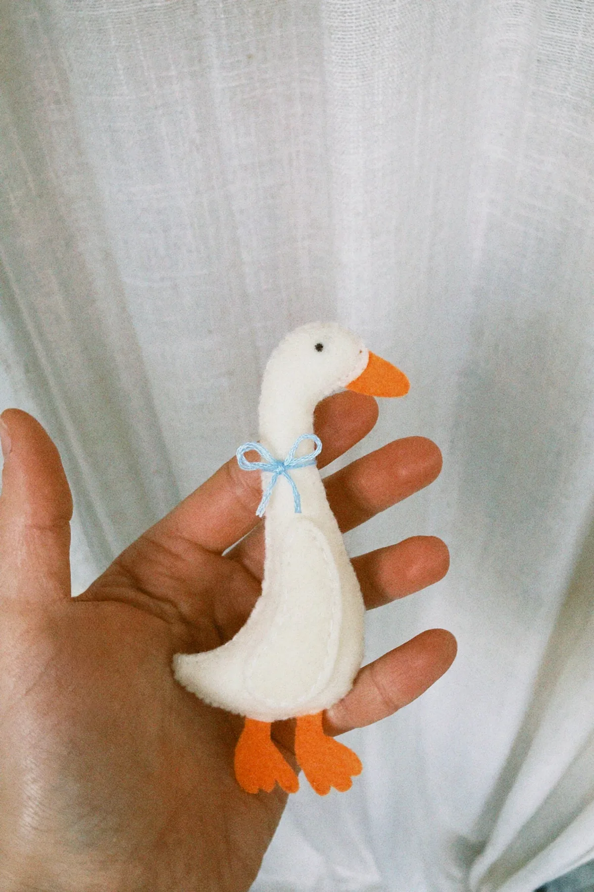 Een vilten gans met een blauw strikje op de hand van Hilda